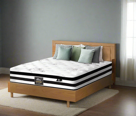 Bed with pillows and a mattress on a wooden bed frame against a green wall with a plant and artwork.