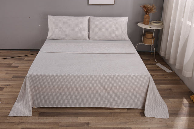 Gray textured bedspread on a bed in a room with wooden flooring and a small table.